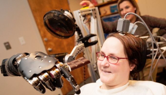 Em 2012, Jan Scheuermann, tetraplégica, usou interface cérebro-máquina para controlar um braço mecânico e comer chocolate por conta própria (Crédito: University of Pittsburgh Medical Center)