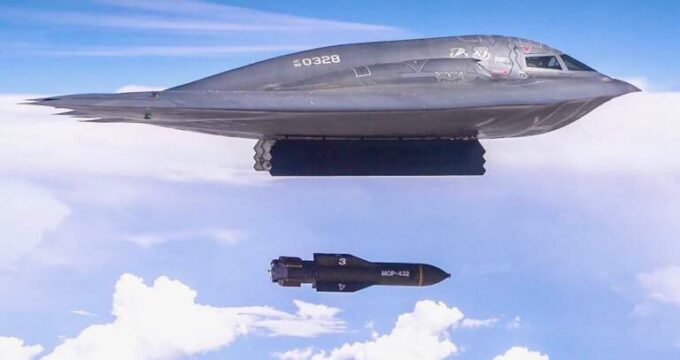 A imagem mostra um jato de caça voando no céu. O jato é de cor cinza e possui o número "0328" escrito ao lado. Tem um nariz pontudo e uma cauda pontiaguda. Em frente ao jato, há um míssil preto com o número 3 nele. O míssil parece estar voando em alta altitude. O céu é azul com nuvens brancas ao fundo.